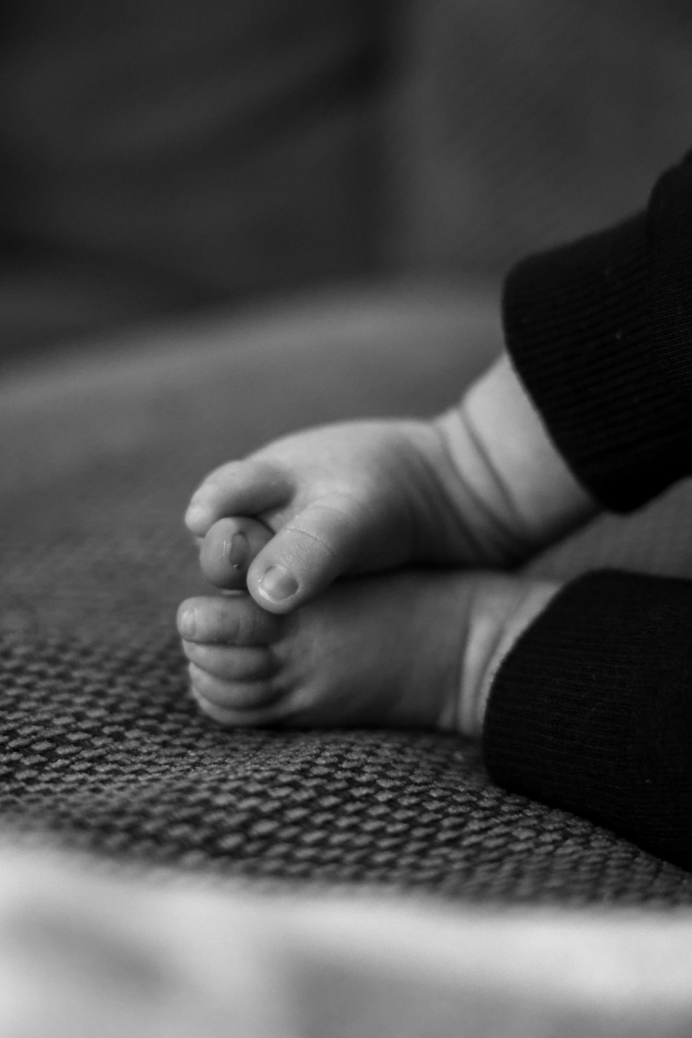 Close up black and white image of tiny baby feet resting on textured fabric.