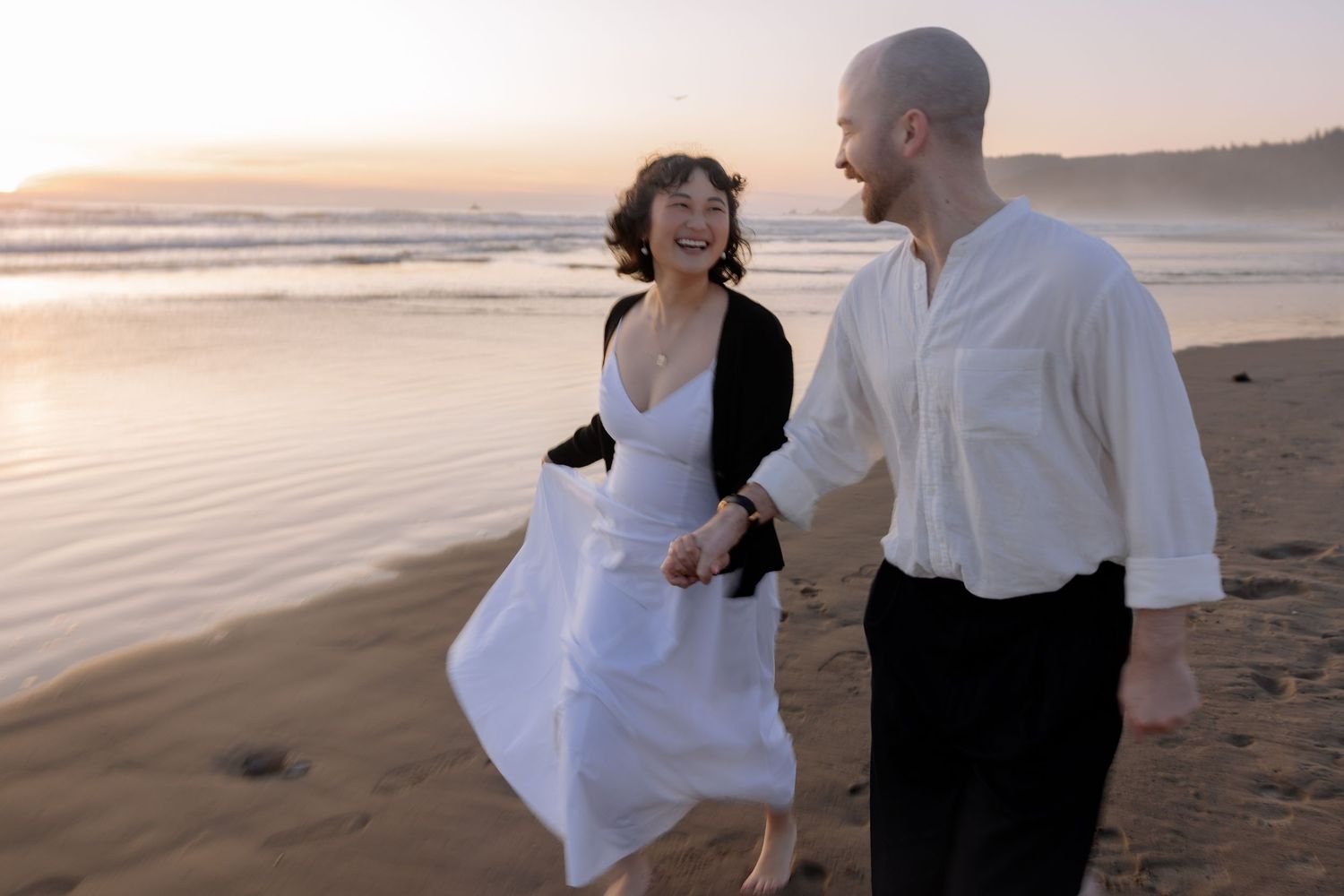 A couple shares a playful moment while walking along the beach at sunset.