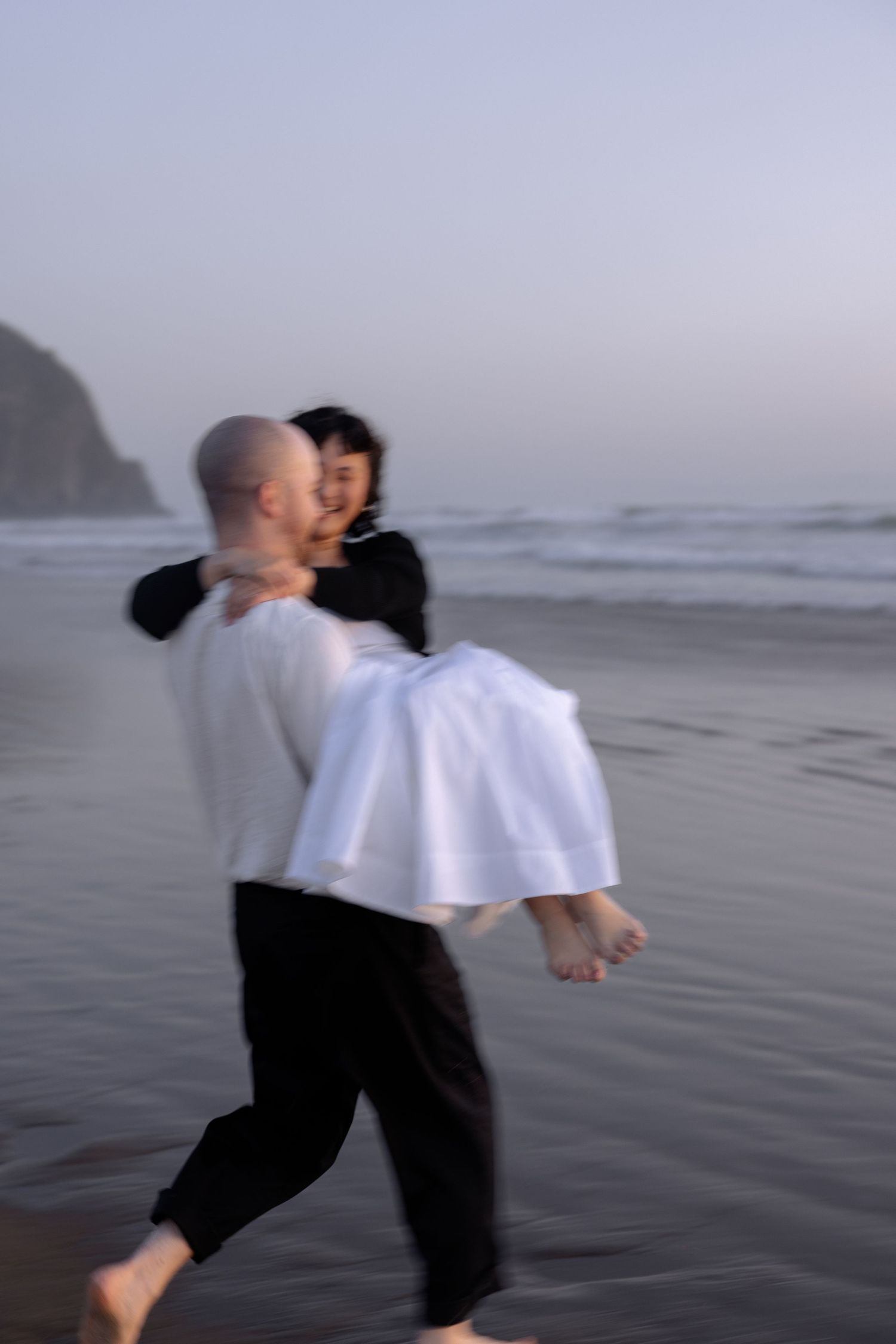 A couple dances playfully together on a wet sandy beach.