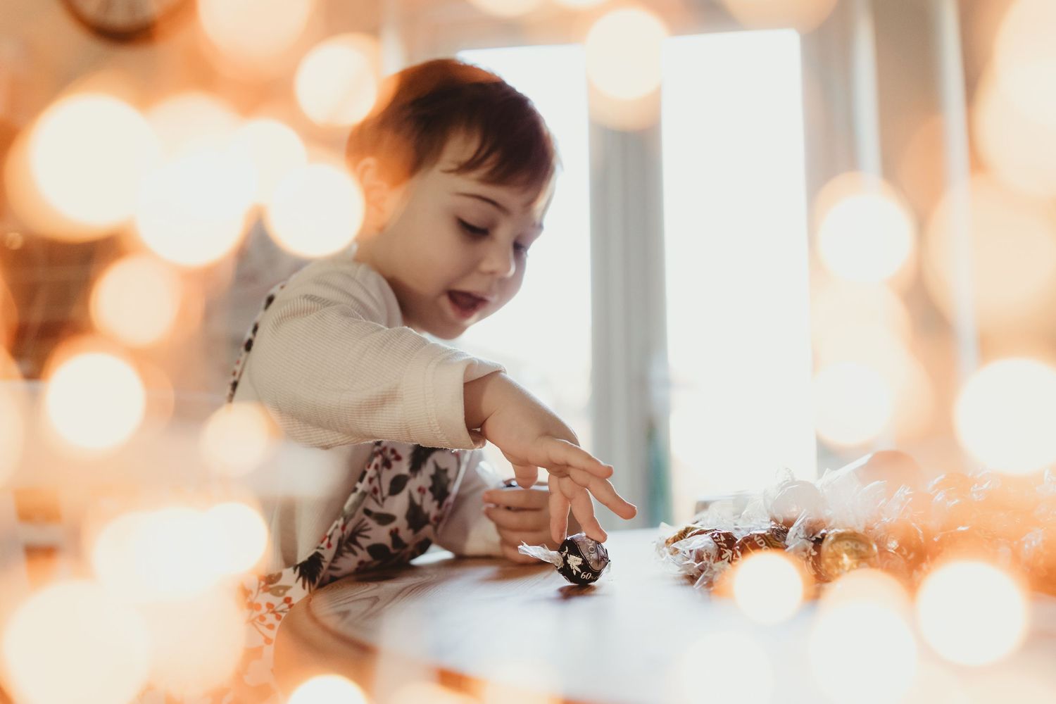 A young child in a white dress plays with toys while surrounded by soft bokeh lights in a dreamy setting.
