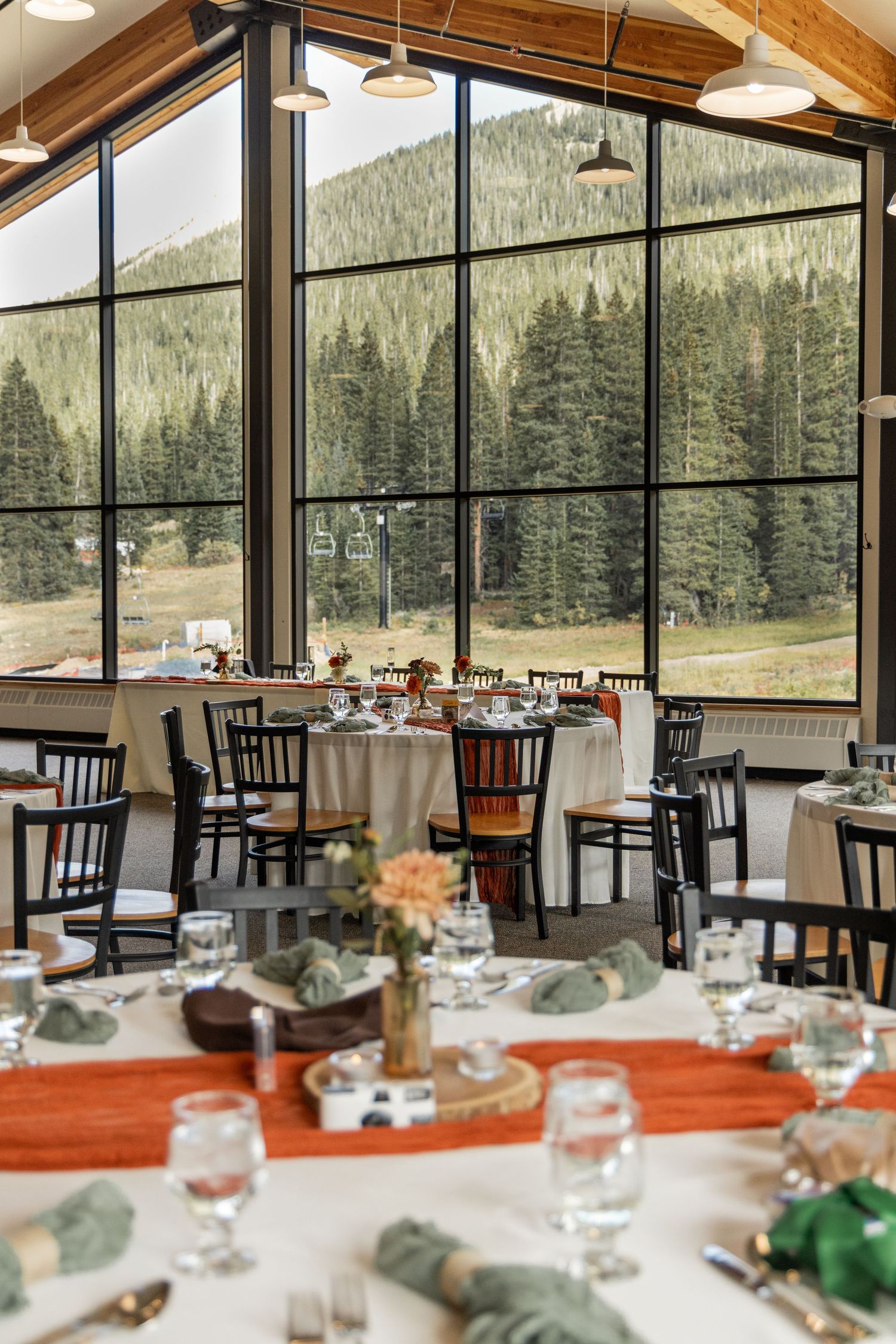 Modern mountain lodge restaurant with floor-to-ceiling windows offering panoramic forest views and elegant table settings.