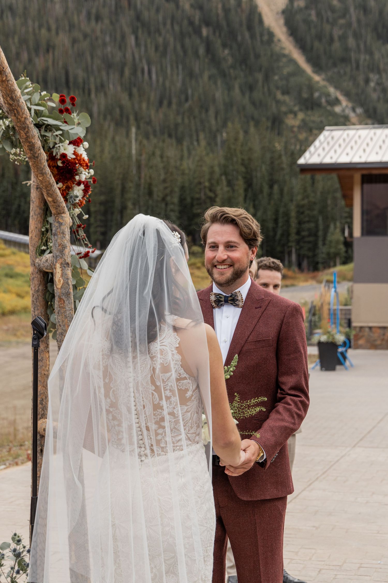 A couple shares a romantic moment during their outdoor mountain wedding ceremony in a burgundy suit and white dress.