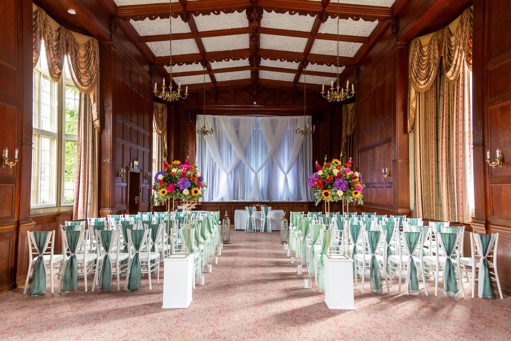 Elegant rustic Tylney Hall interior event venue with exposed beams and white drapes features rows of tables set for a wedding reception.