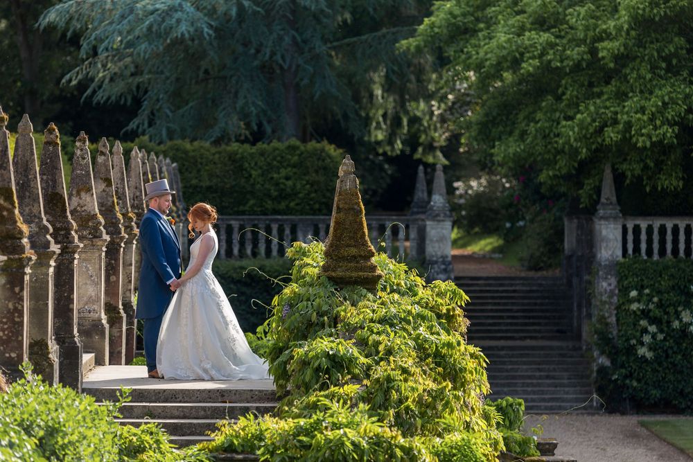 Wedding couple walks hand in hand through a lush garden pathway surrounded by greenery and stone steps at Tylney Hall