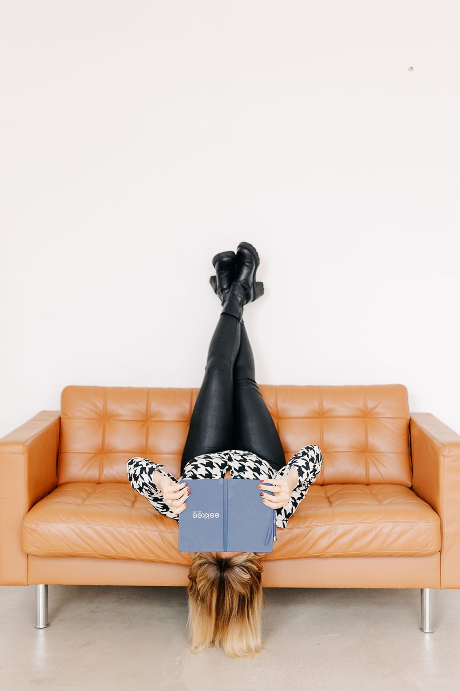 Person lying upside down on tan leather couch in creative photo series showing different lounging positions.