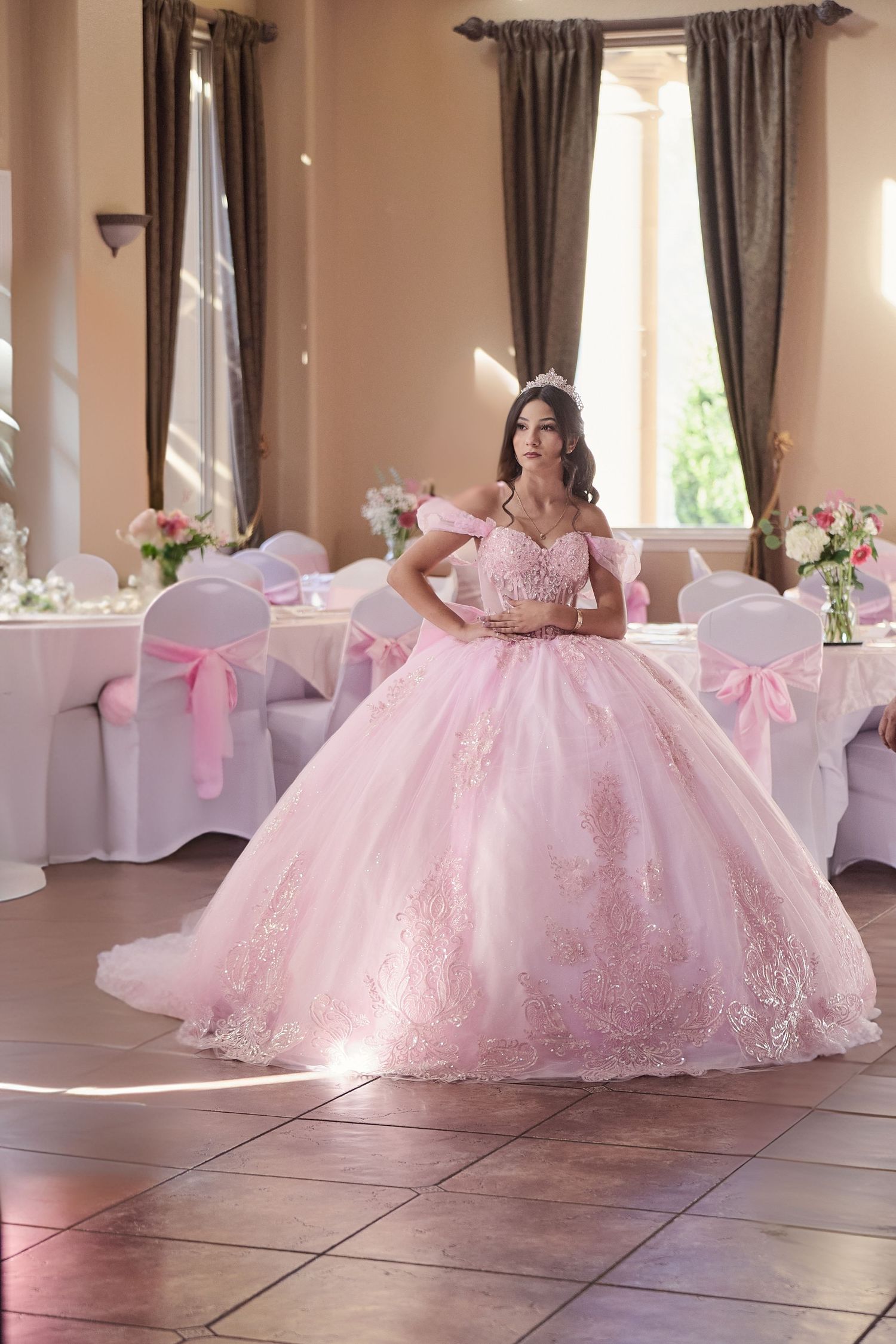 Beautiful pink ball gown with lace details and bow accents photographed in an elegant event venue with white chair covers.