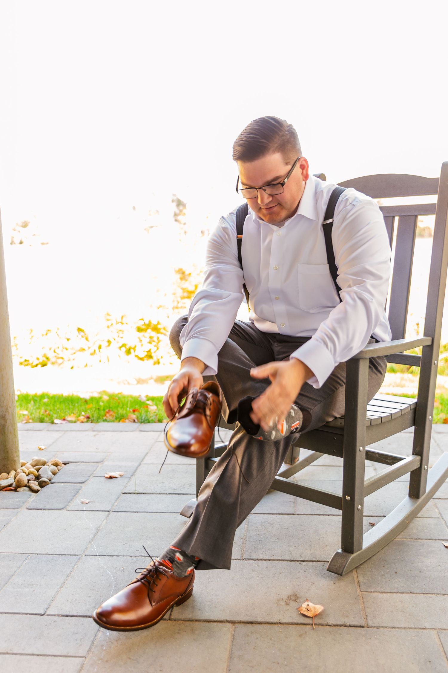 Person in formal attire sitting on a porch tying brown leather dress shoes in a sequence of steps.