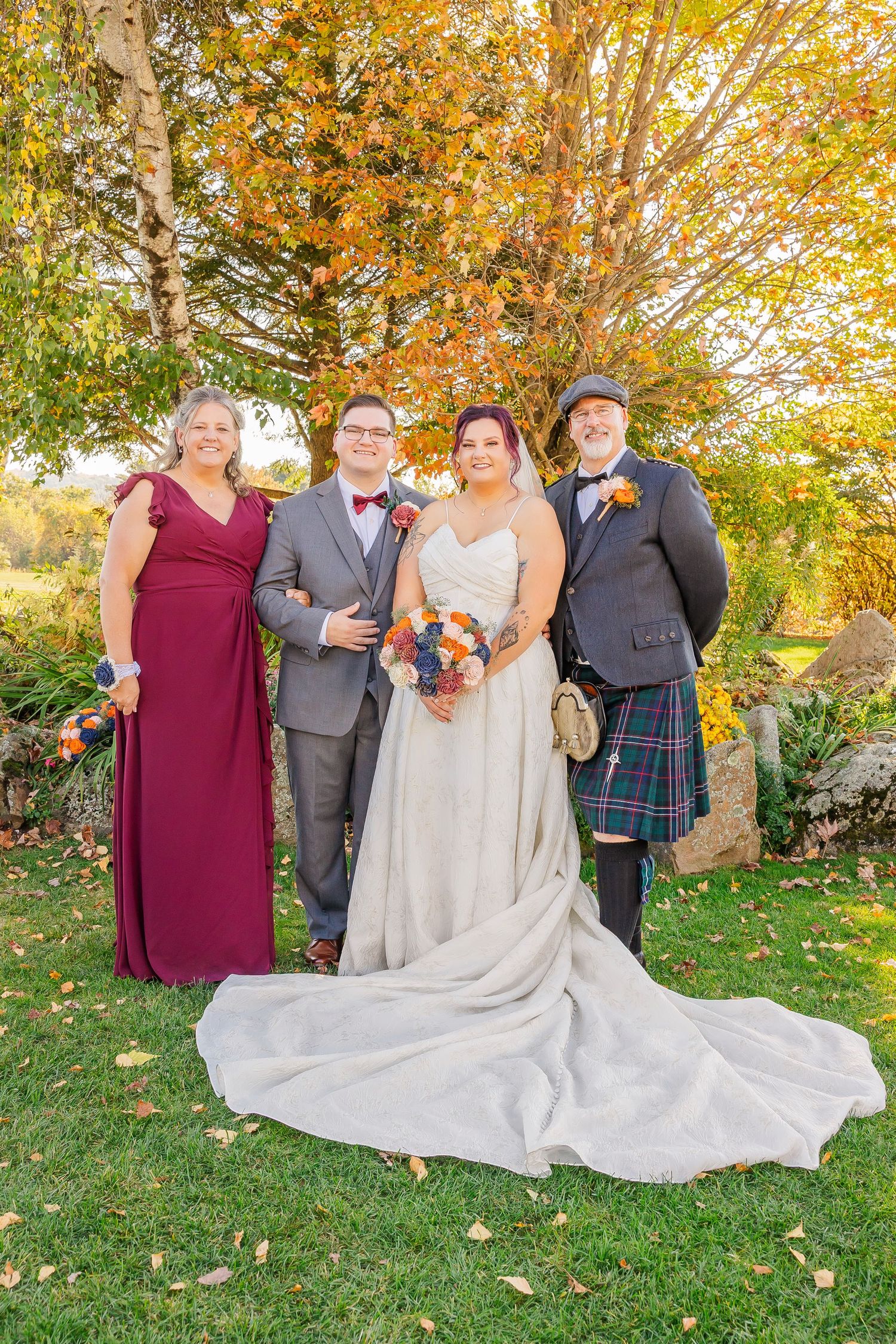 Wedding party poses together on lawn with autumn foliage and fallen leaves creating a warm seasonal backdrop.