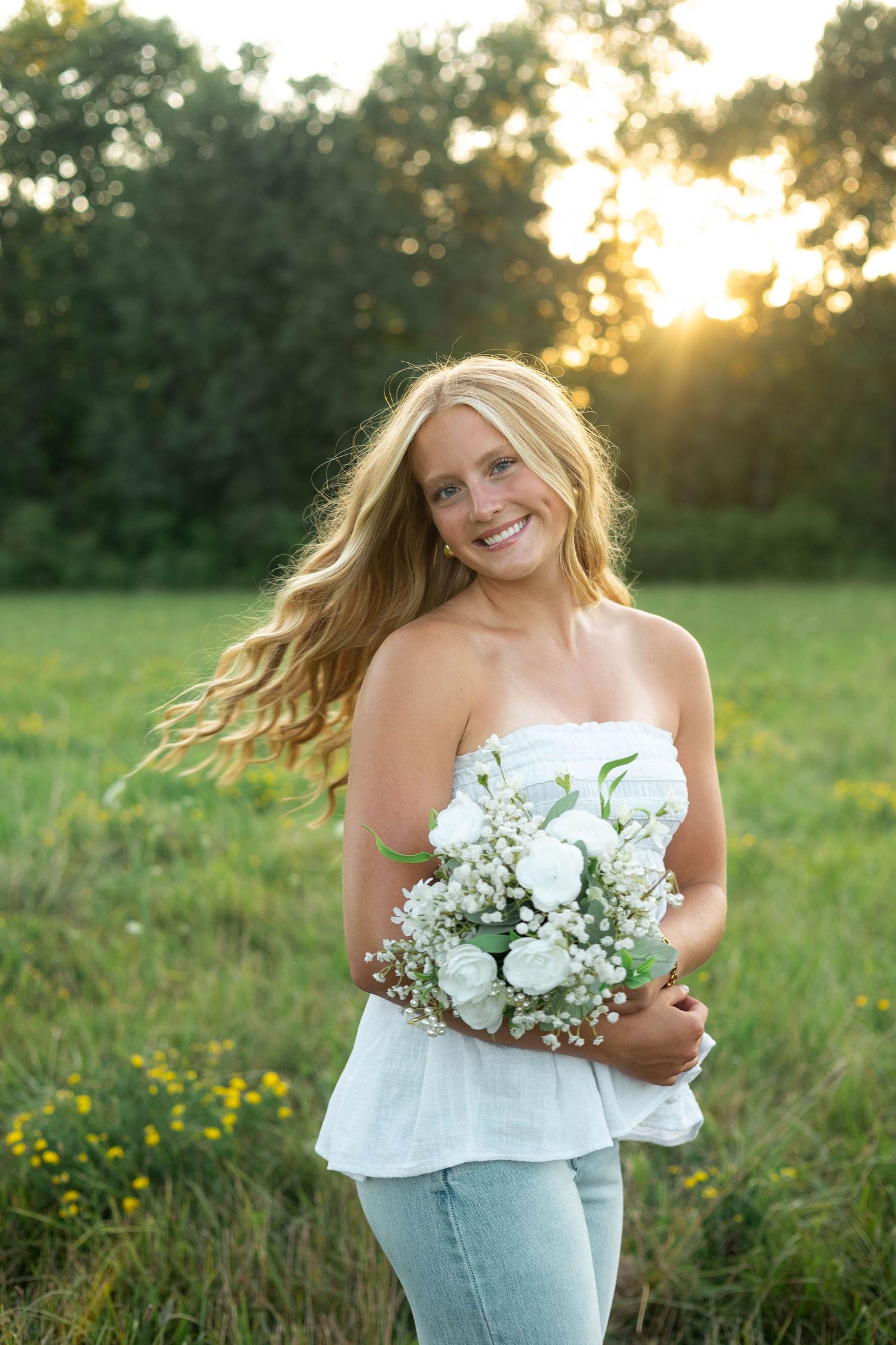 Senior girl carrying a bouquet of flowers through a sunny field during a senior photography session in Northwestern Pennsylvania.