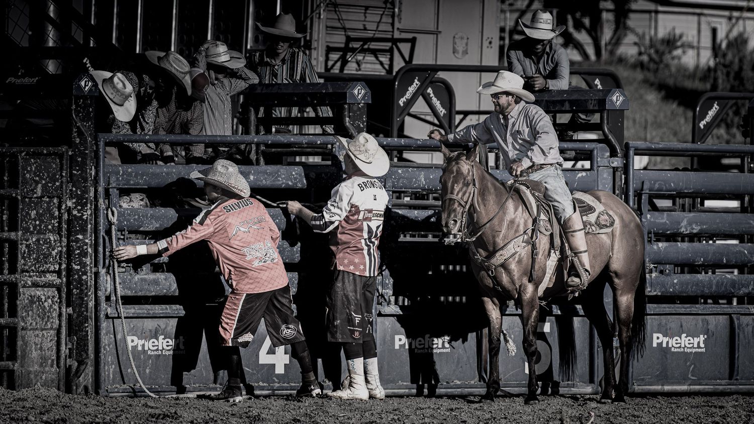 Western rodeo scene with spectators watching from behind fence.
