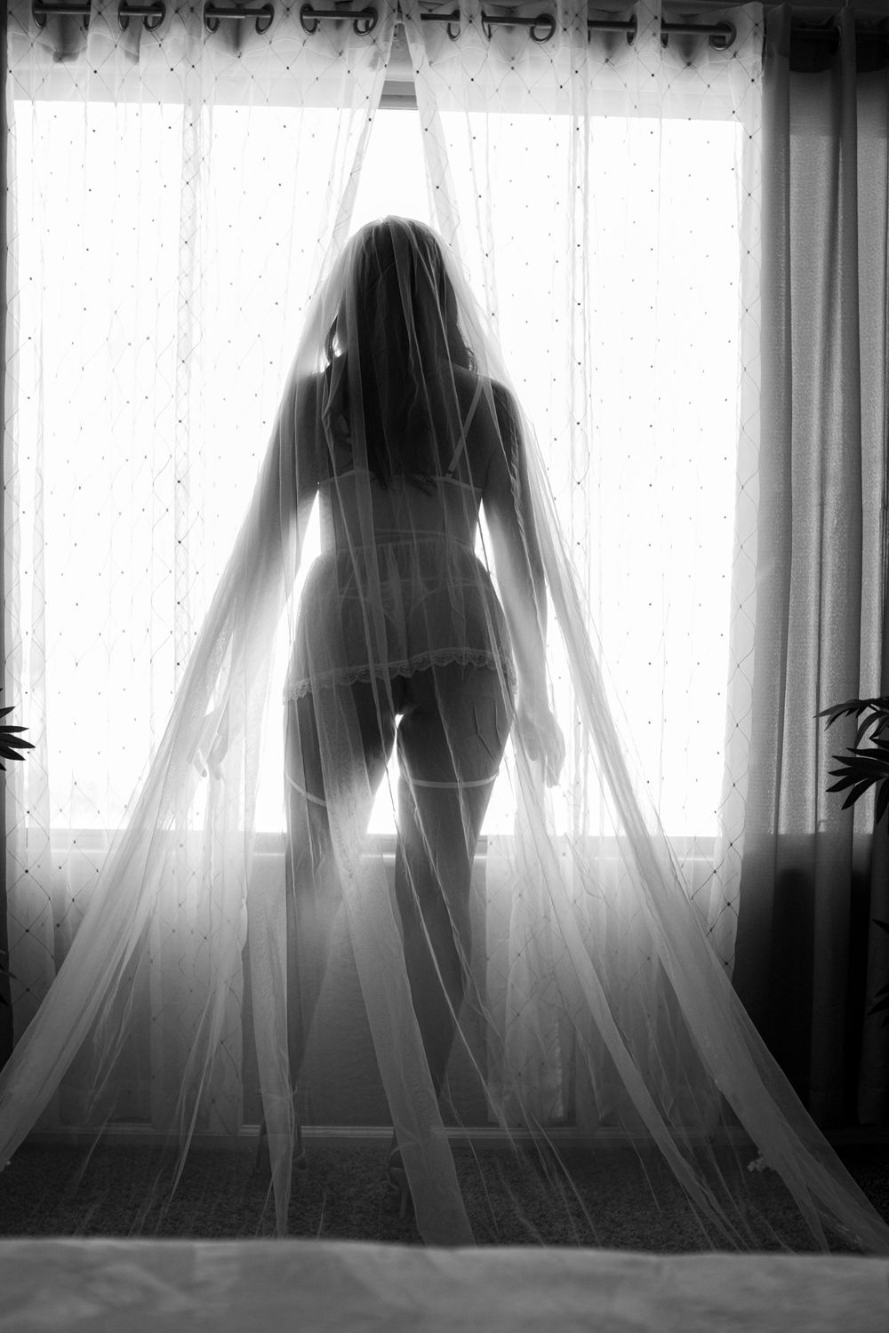 Silhouetted figure stands behind sheer white curtains in a haunting black and white photo series.