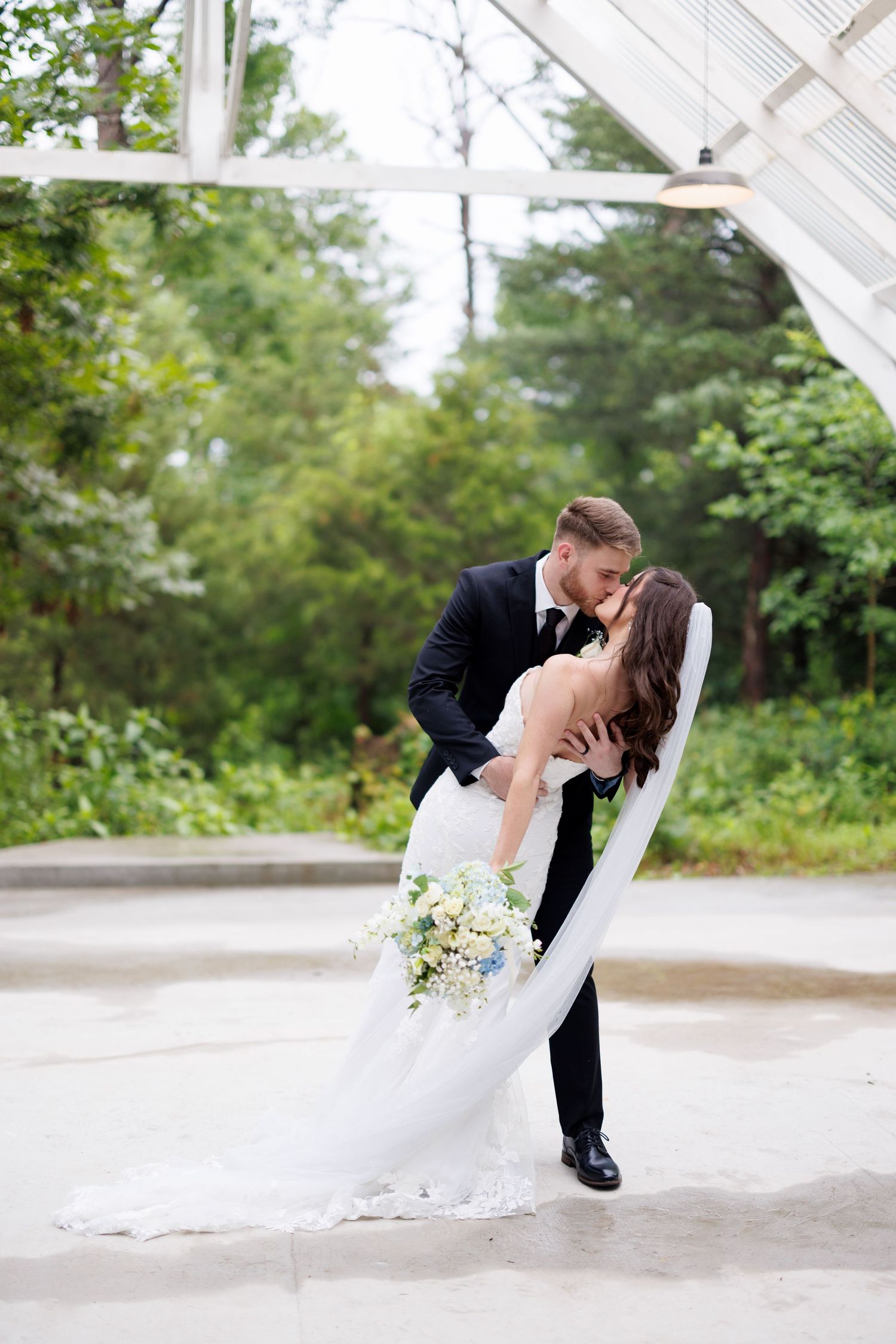 Romantic dip pose of newlyweds outdoors with white floral bouquet.