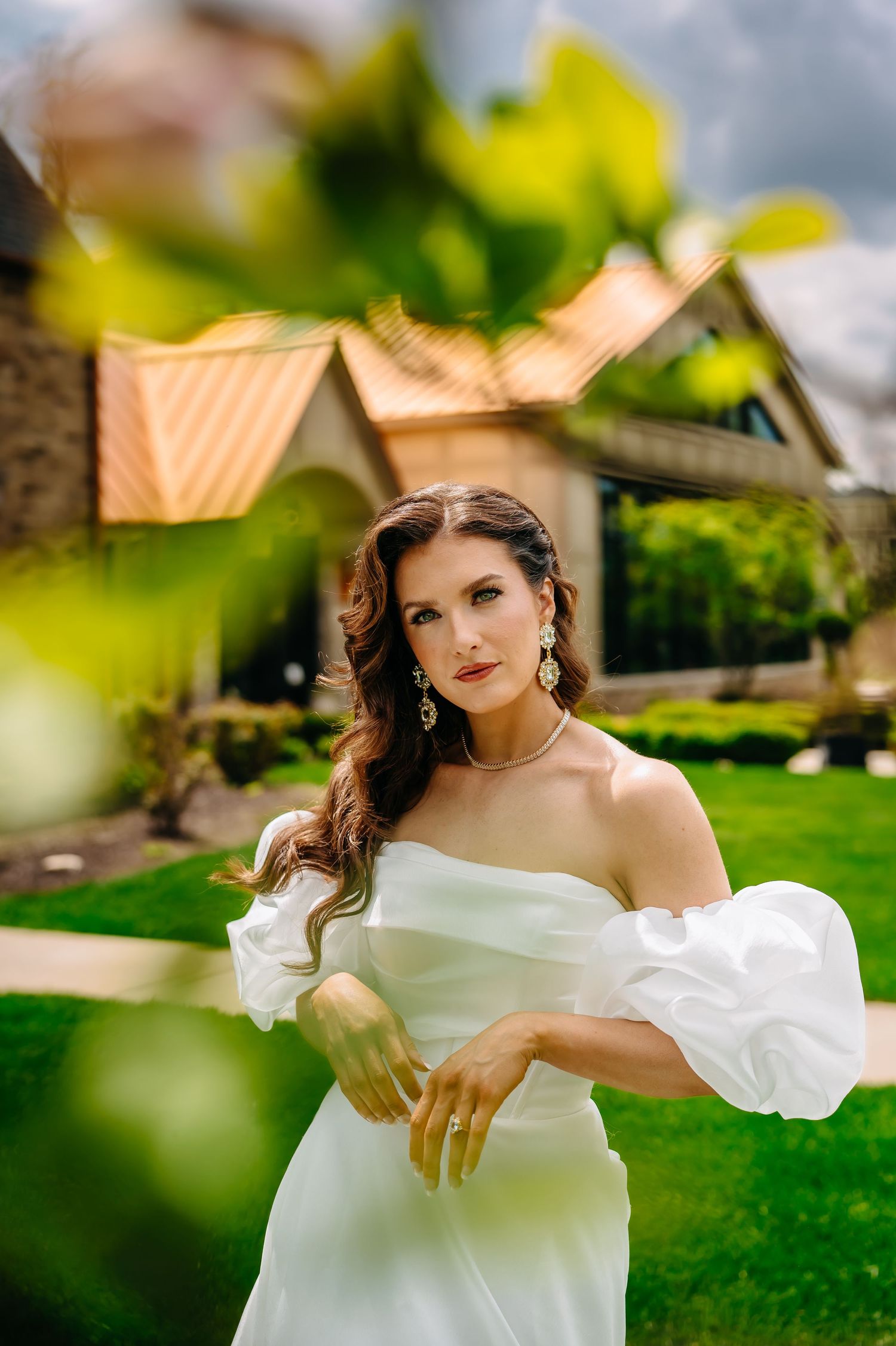 A person in an elegant white off-shoulder dress poses gracefully on a lush green lawn with soft natural lighting.