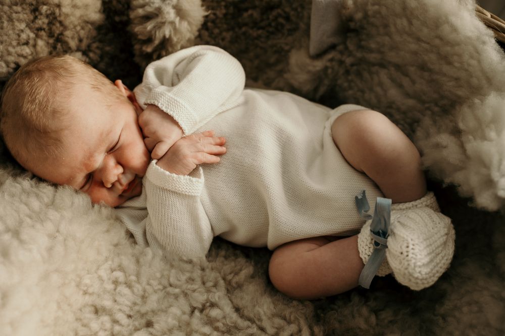 Four tender newborn portraits showing tiny details of sleeping baby against soft white textured backdrop.