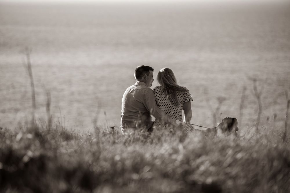 A couple shares a romantic moment sitting together in a golden field with their dog nearby.