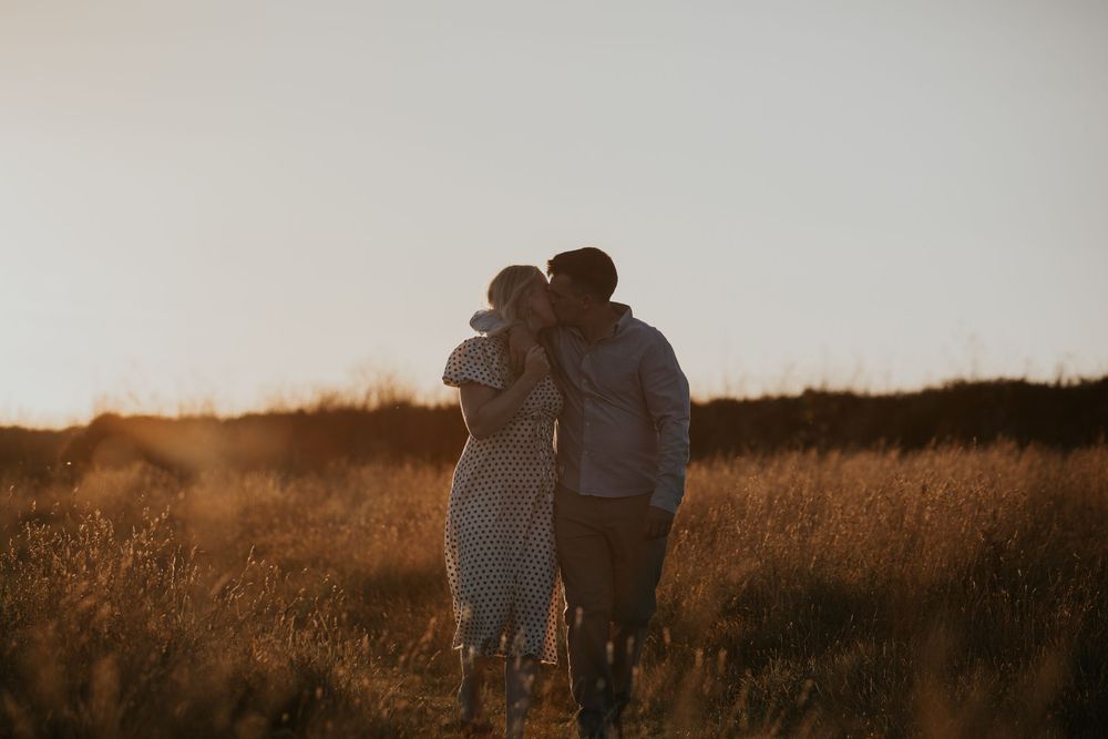A couple embraces in a sun-drenched golden field at sunset, sharing a tender romantic moment.