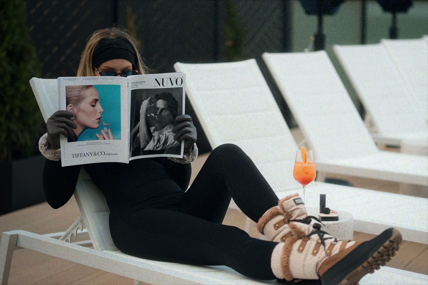 a woman in boots laying on a subbed reading a fashion magazine.