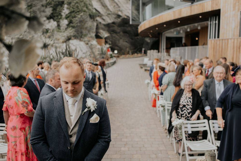A groom in a navy suit waits anxiously at the altar during an outdoor wedding ceremony.