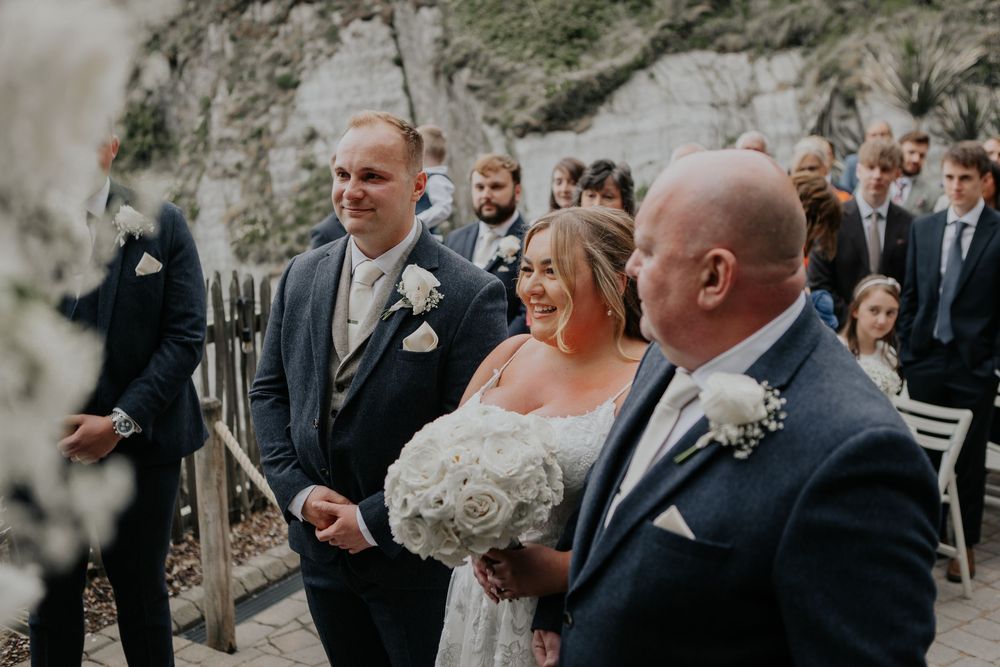 A bride smiles joyfully as she meets the groom at the altar during an outdoor wedding ceremony.