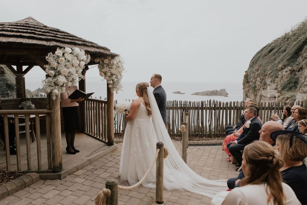 Bride and groom exchange vows under floral arch gazebo at stunning cliffside outdoor wedding ceremony by the sea.