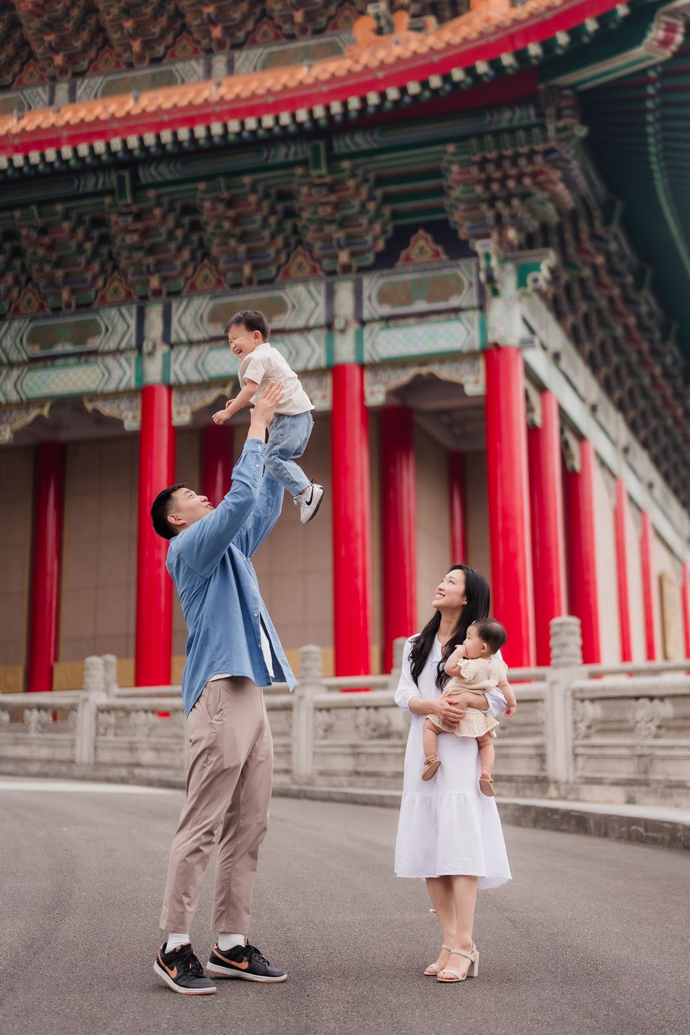 A family poses playfully in front of traditional Chinese architecture with red pillars and ornate details at CKS Memorial Hall, Taipei.