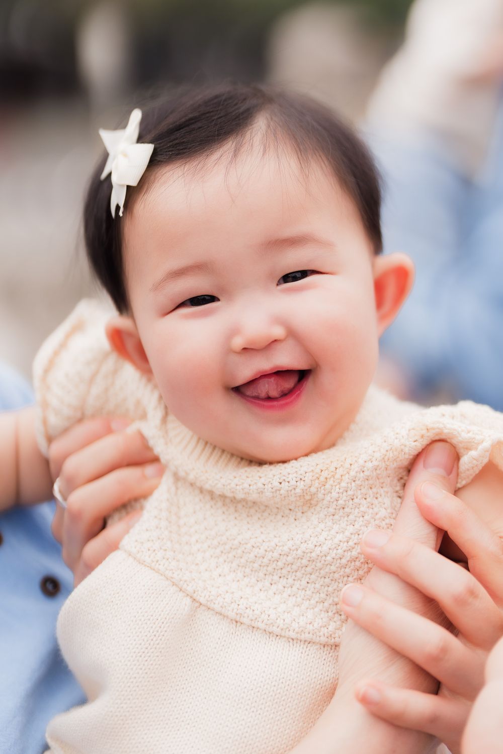 Close-up sequence of a smiling baby girl wearing a cream-colored knit sweater with a white hair bow.