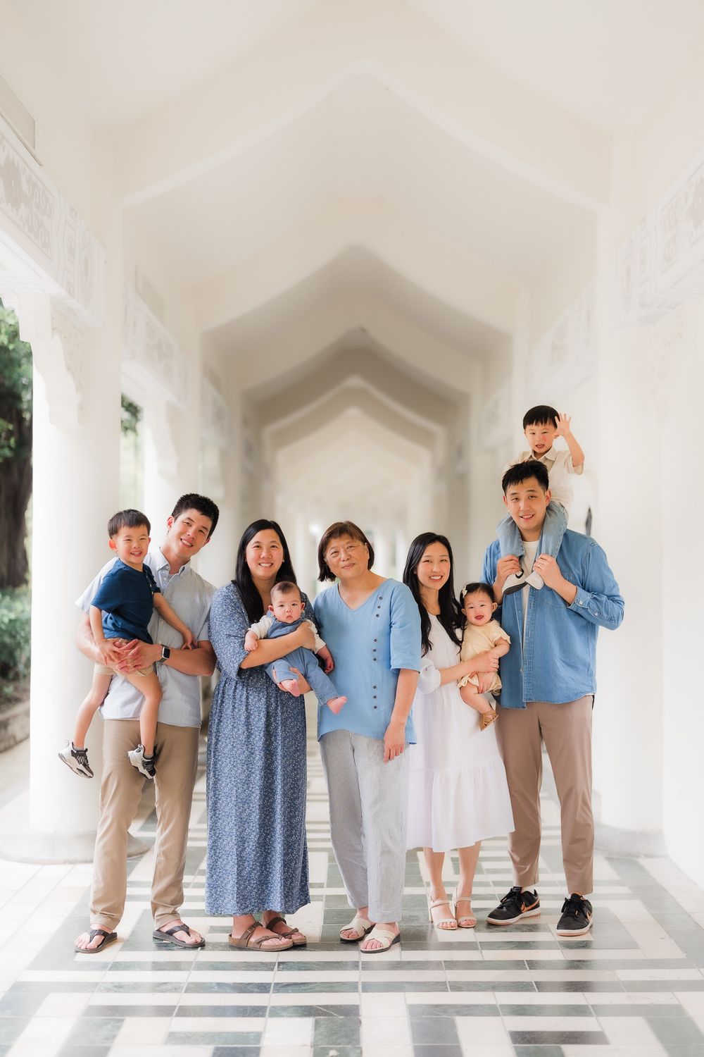 Extended family wearing coordinated blue and white outfits poses together in an elegant white archway in Taipei, Taiwan.