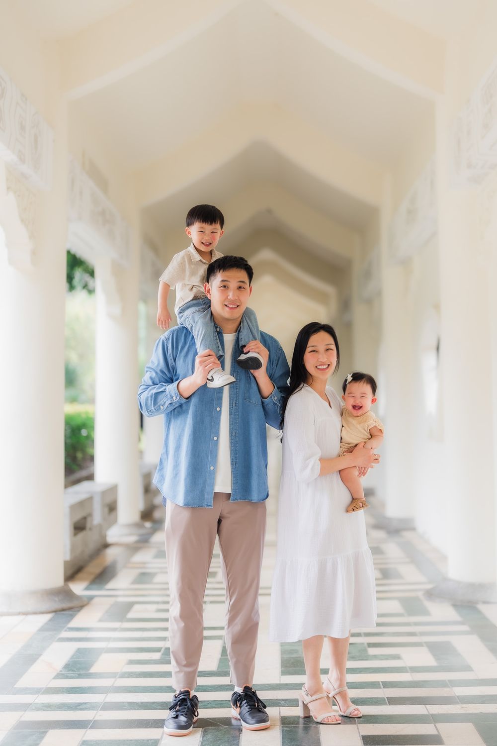 Family portrait walking through a white architectural colonnade with arches accented by soft white light shining through the pillars.