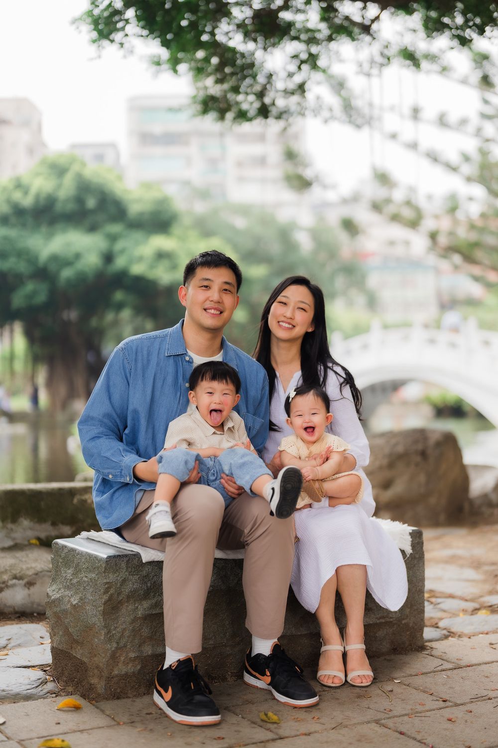 A family sits on a stone park bench with draping tropical greenery in the background at Chiang Kai Shek Memorial Hall garden, Taipei.