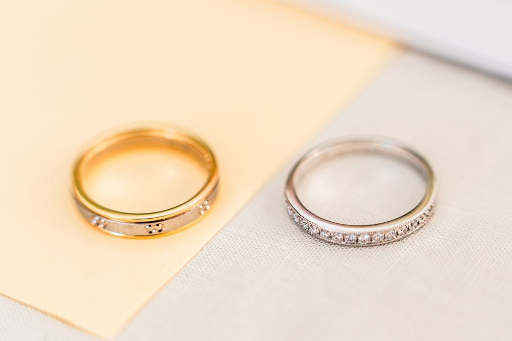 Two wedding rings in gold and silver with diamonds sit on a soft beige surface in natural light.