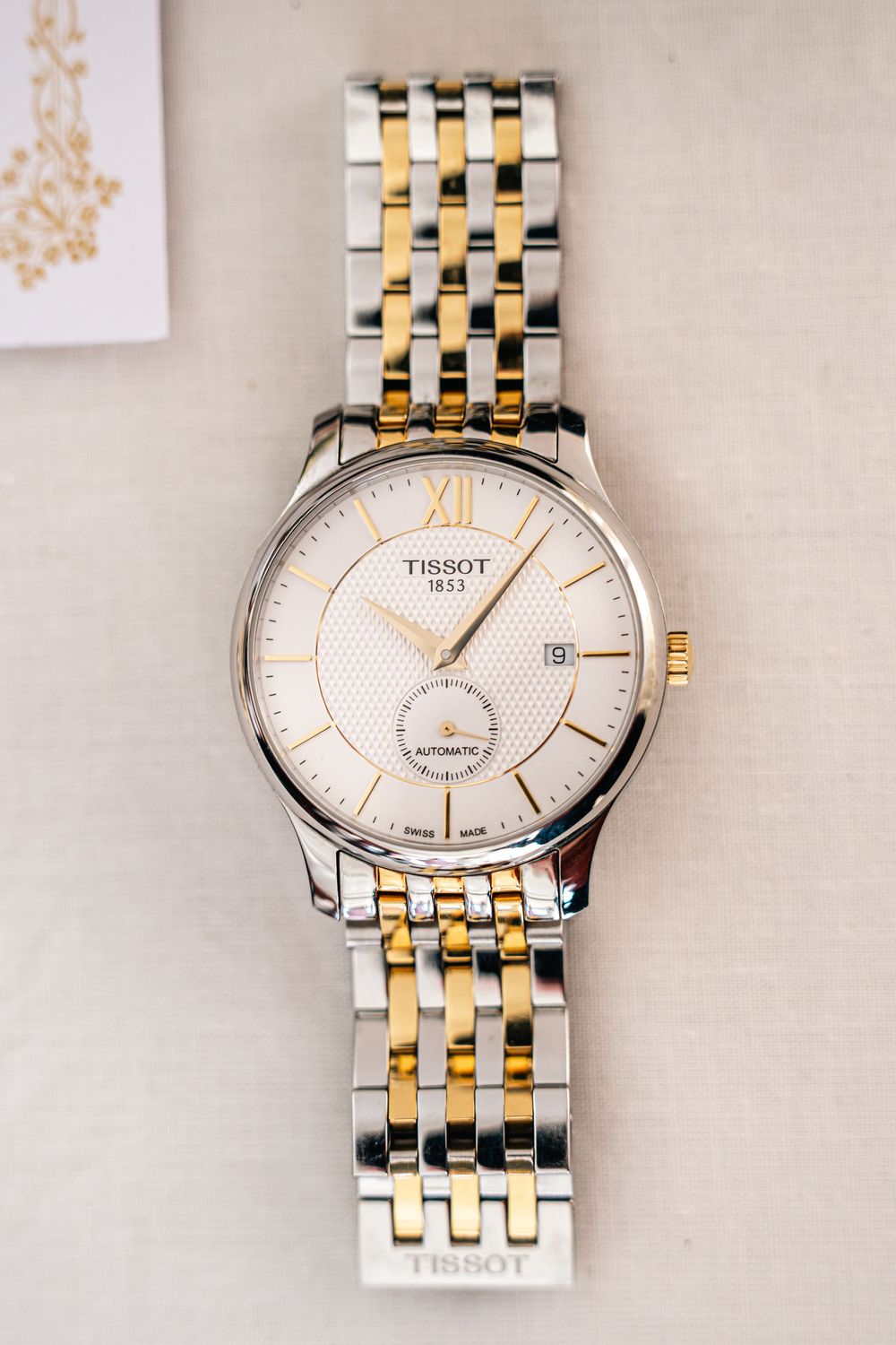 Two-tone Tissot watch with gold and silver link bracelet displayed on light background.