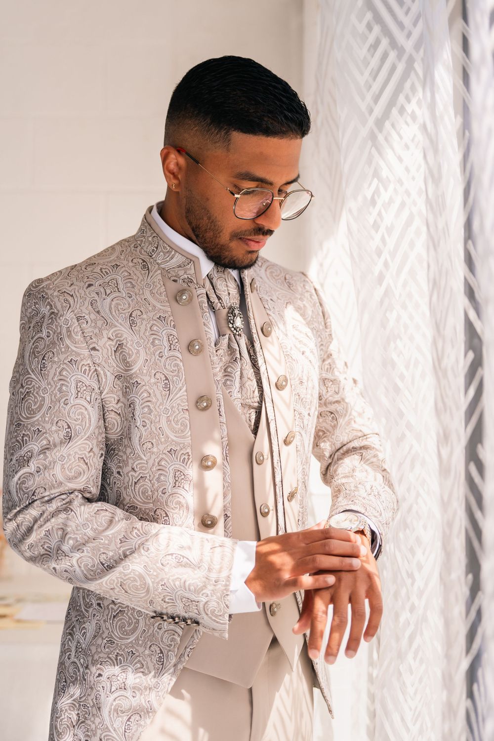 A groom in an elegant white and silver paisley suit adjusts his cuffs before the ceremony.
