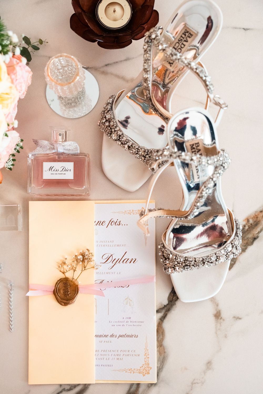 Elegant wedding details including perfume bottles, invitations and decorative accessories on a marble surface.