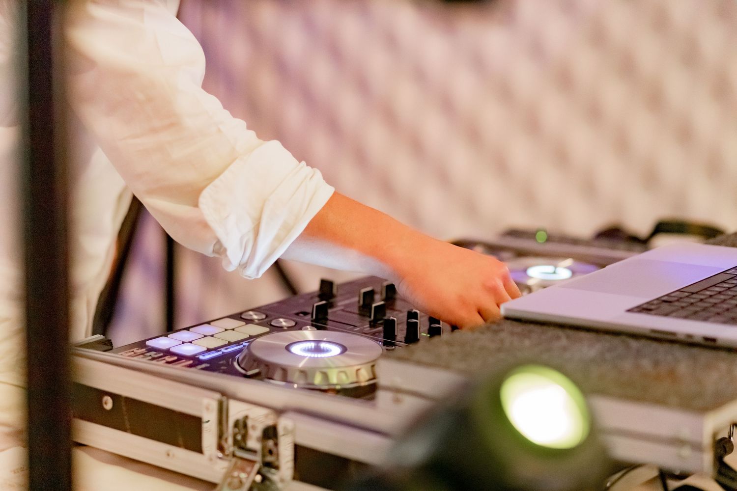 DJ mixing music on a professional controller with laptop and mixer equipment in a nightclub setting.