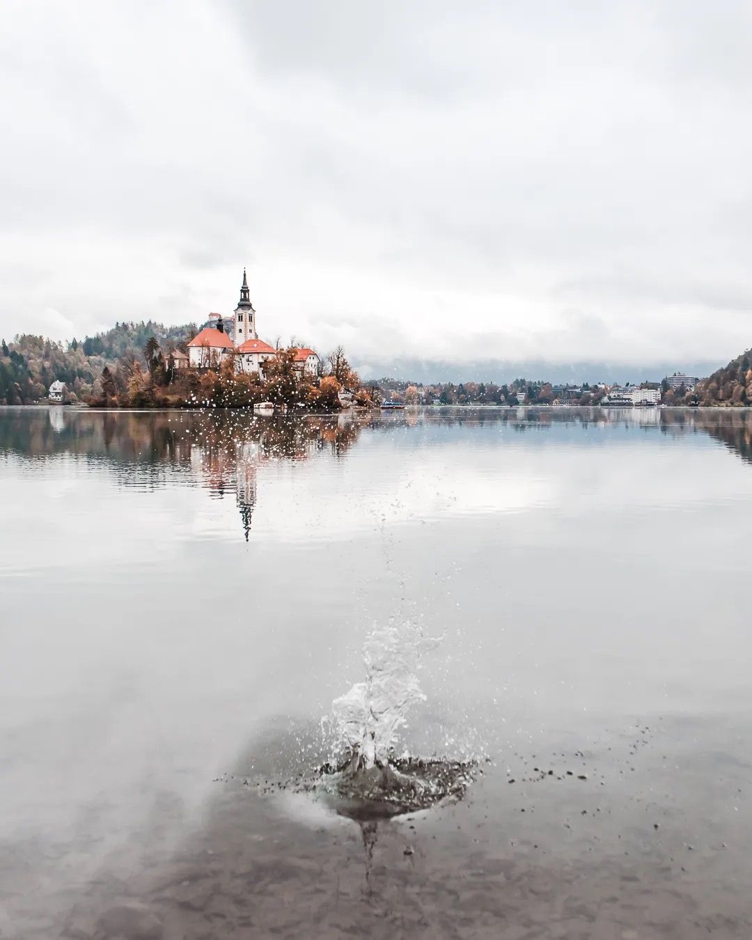 Lake Bled church reflected in calm water on a misty morning.