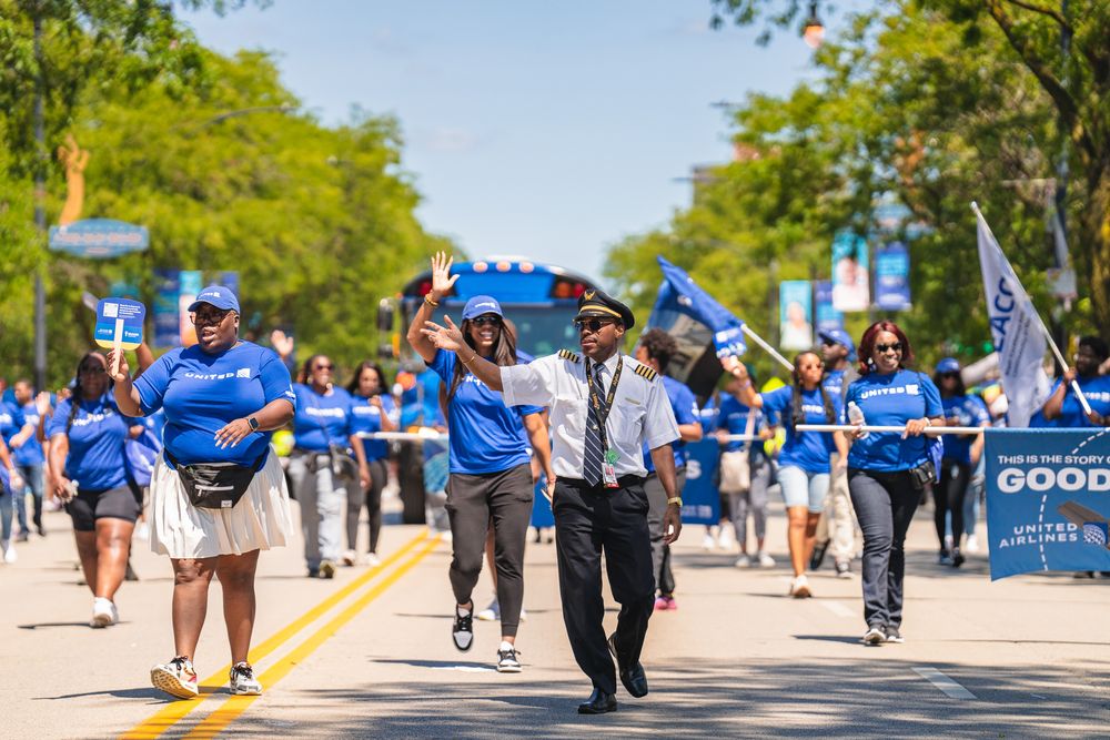 People walking along sunny outdoor path with blue banners and trees.