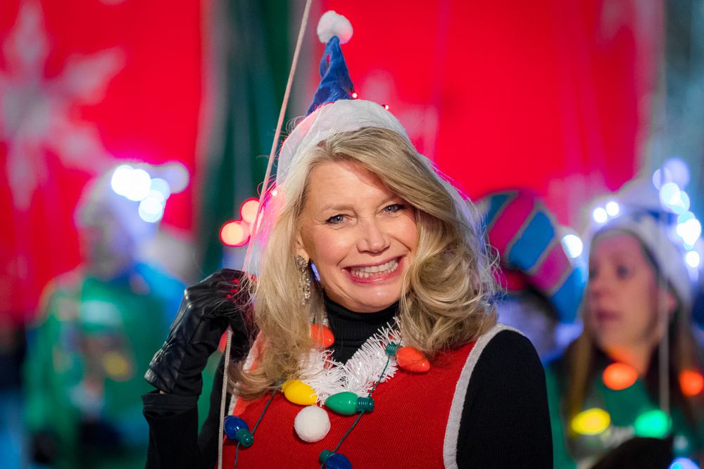 A festive holiday scene with someone wearing a red sweater and blue party hat amid twinkling lights.