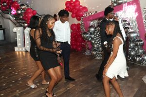 Group of party guests dancing together near red and silver balloon decorations.