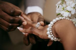 Close-up of hands exchanging rings with pearl bracelet detail.