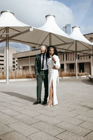 A couple stands under modern white canopy structures in formal wedding attire.