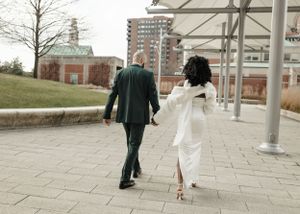 A couple walking hand in hand under outdoor canopies in formal attire.