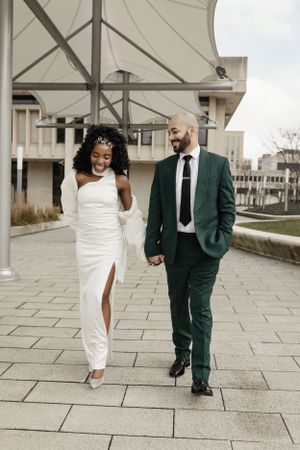 A couple walking together on a paved pathway in formal wedding attire.