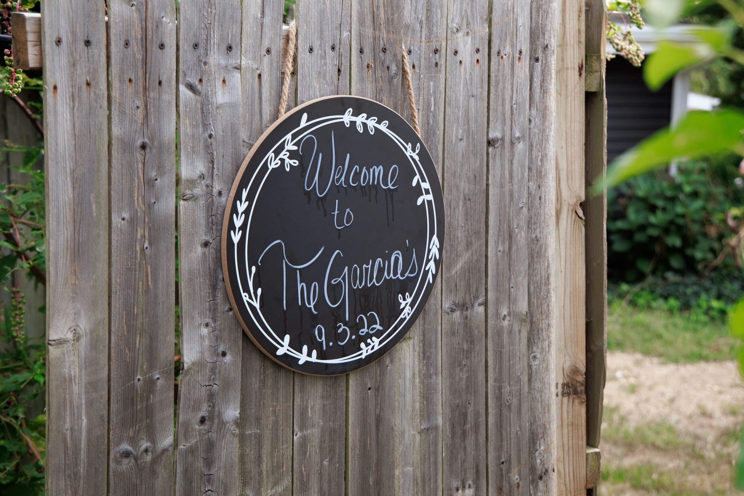 Rustic wooden fence with decorative round chalkboard sign for wedding ceremony.