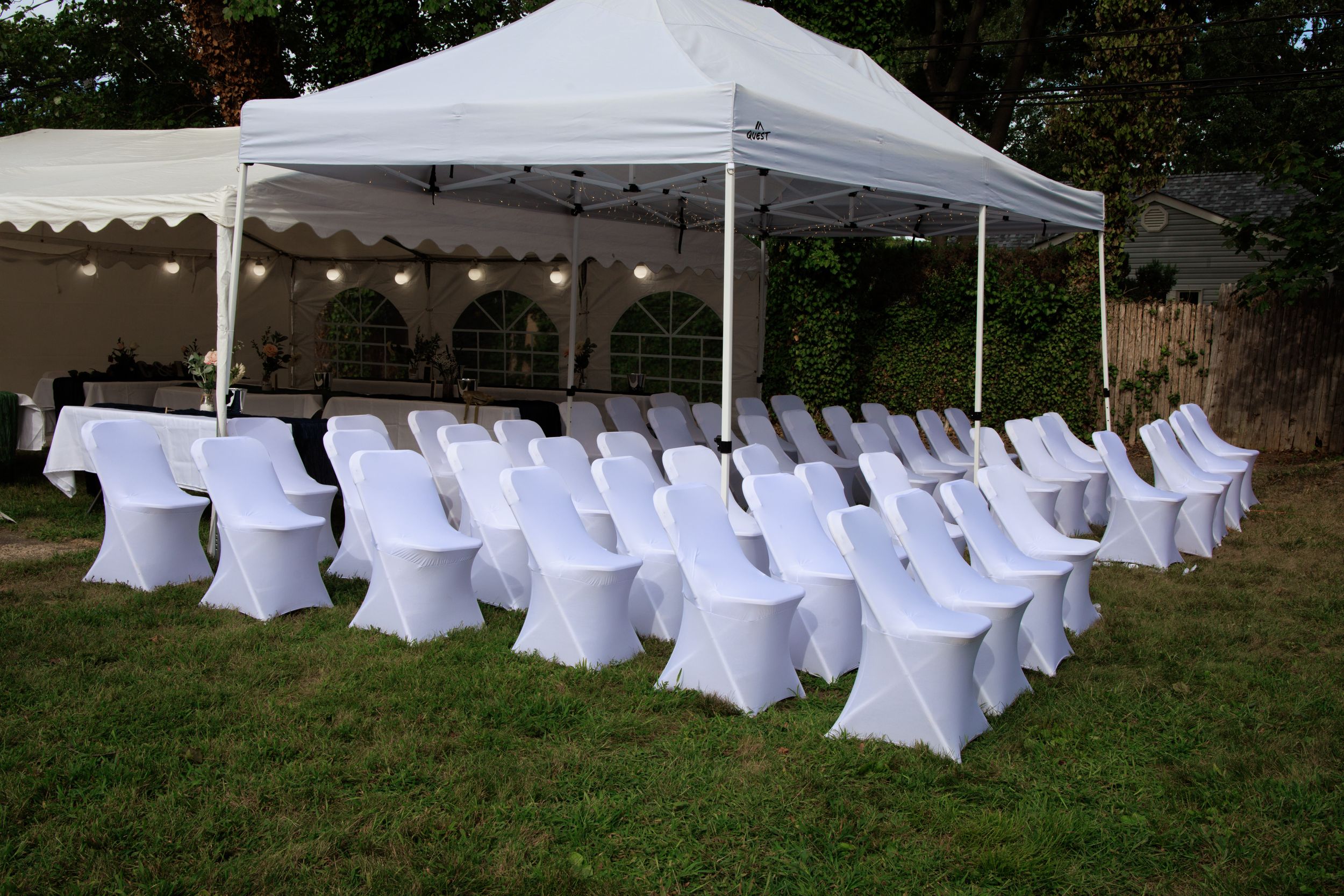 White folding chairs arranged in rows under a wedding ceremony tent on a lawn.