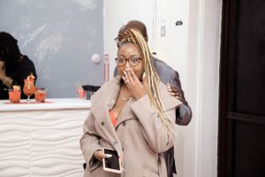 Person in a beige coat expressing surprise with their hand over their mouth at an event.