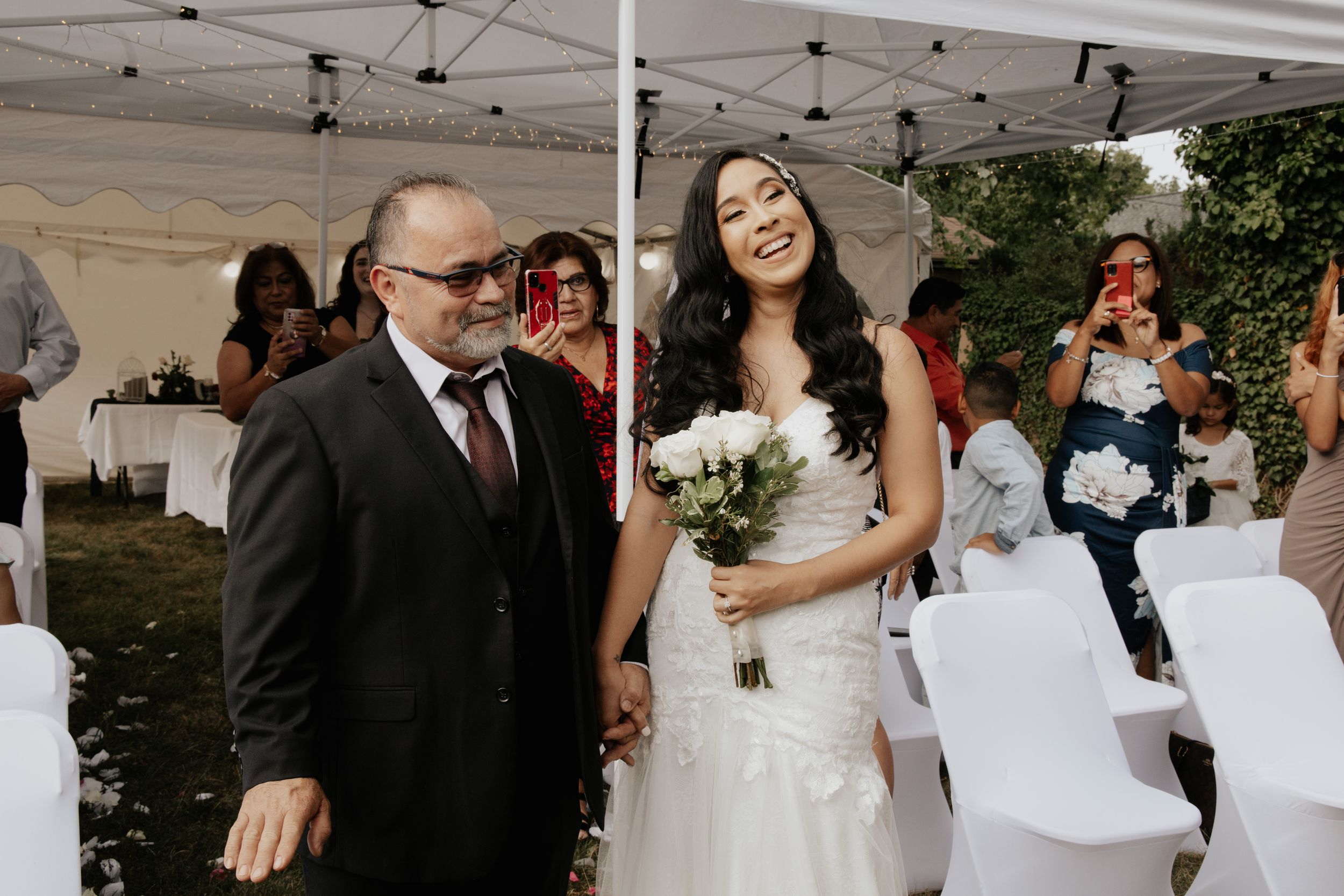 Wedding ceremony seating area with white chairs and guests gathering under a tent.