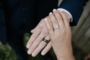 Close-up of newly married couple's hands showing their wedding rings against a dark suit.