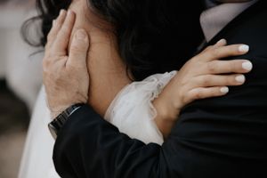 Intimate embrace between newlyweds with focus on hands and formal attire.