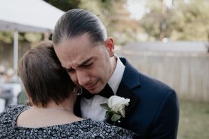 Emotional wedding moment showing tender embrace with groom wearing navy suit and white boutonniere.
