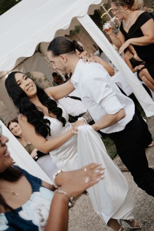 Joyful dance celebration at a wedding reception under a white tent outdoors.